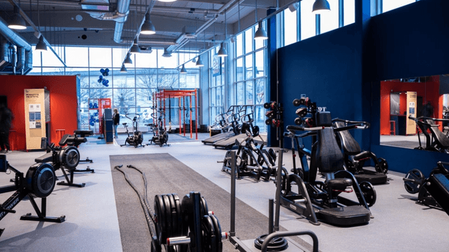 Ett modernt och rymligt gym från Fitness 24 Seven med styrketräningsmaskiner, roddmaskiner, battleropes och stora fönster.
