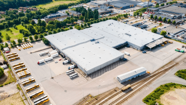 Flygfoto i fågelperspektiv över ett storskaligt logistikcenter och bussdepå med tillhörande lasthallar, parkeringar och järnvägsspår