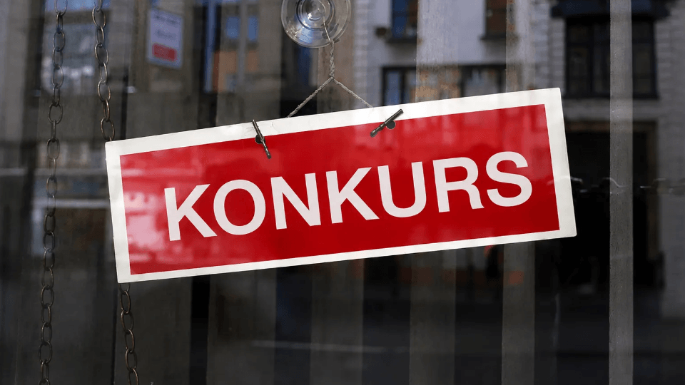 En röd skylt med den vita texten "KONKURS" hängande i ett skyltfönster.