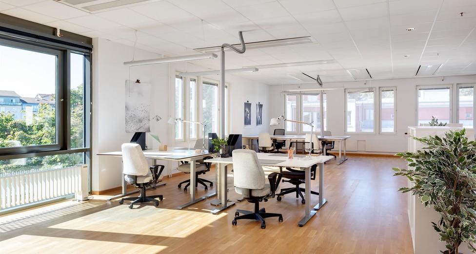 Luftigt rum med arbetsplatser och stora fönster.